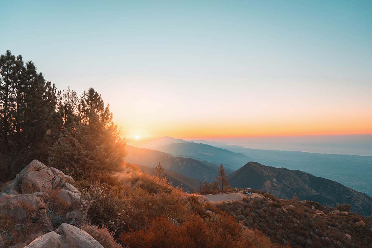 Experience the breathtaking beauty of a mountain summit bathed in golden hour light. This stunning photograph captures the peak stones nestled in a lush green grass field, surrounded by majestic trees as the sun sets in the background. Perfect for travel blogs, outdoor adventure websites, and nature-themed projects, this image evokes a sense of tranquility and the splendor of natural landscapes.